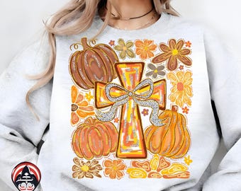 May include: A light gray sweatshirt featuring a fall-themed design. The design includes a cross with a bow, pumpkins, and flowers in shades of orange, brown, and yellow. The overall style is retro and whimsical.