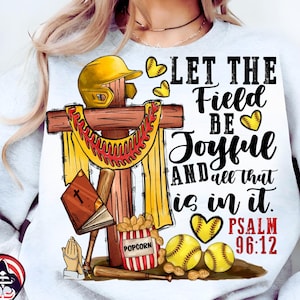Pode incluir: Um moletom cinza claro com um design temático de softball. O design inclui uma cruz de madeira, um capacete de softball amarelo, bolas de softball e o texto "LET THE Field BE Joyful AND all that is in it. PSALM 96:12".