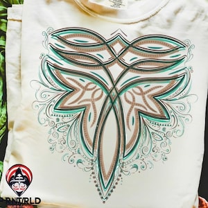 May include: Cream-colored t-shirt featuring a symmetrical floral design in shades of teal and brown. The intricate pattern includes swirling details and a central, elongated shape. The shirt is folded, showing the design prominently.