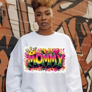 May include: White sweatshirt with a colorful graphic print of the word "MOMMY" with a crown and hearts.
