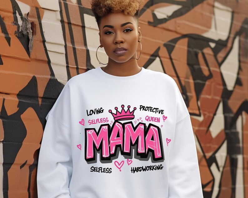 May include: White sweatshirt with a pink and black graphic design that says "MAMA" with a crown above the word and the words "Loving, Selfless, Protective Queen, Selfless, Hardworking" around the word "MAMA".