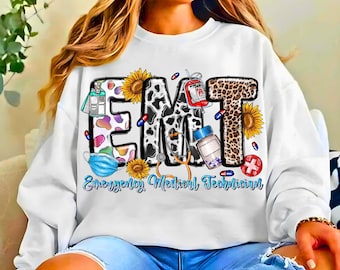May include: White sweatshirt with the letters "EMT" in a cow print and leopard print design. The sweatshirt features medical-themed graphics, including a blood bag, pills, and a stethoscope, with the words "Emergency Medical Technician" in a light blue script.