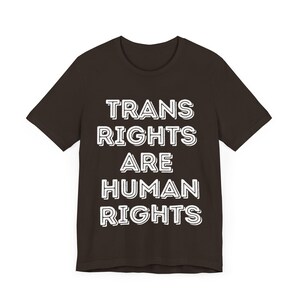 May include: A dark brown t-shirt with white text that reads "TRANS RIGHTS ARE HUMAN RIGHTS".