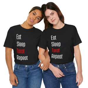 May include: Two black t-shirts with white text that reads "Eat Sleep Tarot Repeat" in a list format. The word "Tarot" is in red.