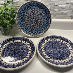 May include: Three ceramic plates with intricate blue floral patterns. The largest plate is round, while the other two are oval-shaped. The plates have a white border and a detailed design with small flowers and heart accents. A decorative piece for the kitchen.