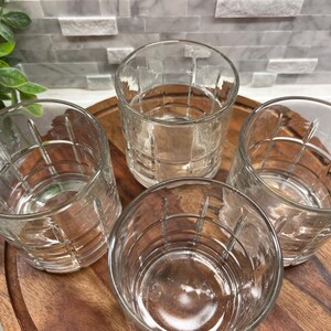 Puede incluir: Cuatro vasos transparentes de vidrio con un patr&oacute;n de cuadr&iacute;cula. Los vasos est&aacute;n sobre una superficie de madera.