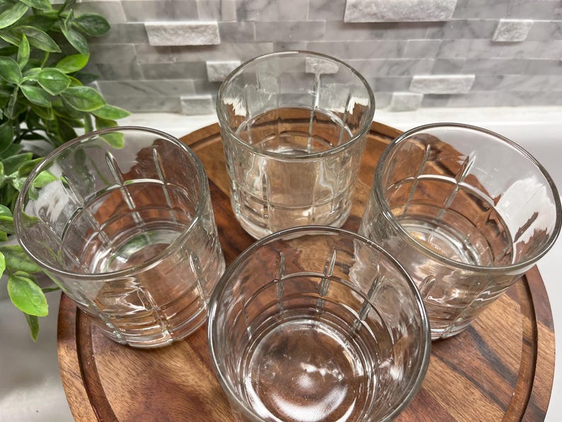 Puede incluir: Cuatro vasos transparentes de vidrio con un patr&oacute;n de cuadr&iacute;cula. Los vasos est&aacute;n sobre una superficie de madera.
