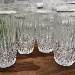 May include: Set of four clear glass tumblers with a diamond pattern. The glasses are empty and sitting on a wooden surface.