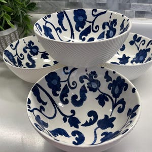 May include: Four white ceramic bowls with a blue floral pattern. The bowls have a textured exterior and a smooth interior. The floral design features stylized flowers and leaves. The bowls are stacked and arranged on a white surface.