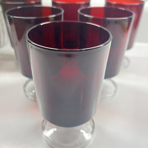 May include: Set of six red glass wine glasses with clear glass stems and bases. The glasses are all the same size and shape.