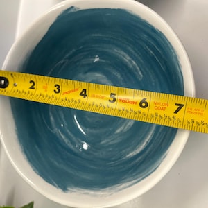 May include: White ceramic bowl with a blue swirl design. A yellow tape measure is placed across the bowl, showing a diameter of approximately 18 cm.