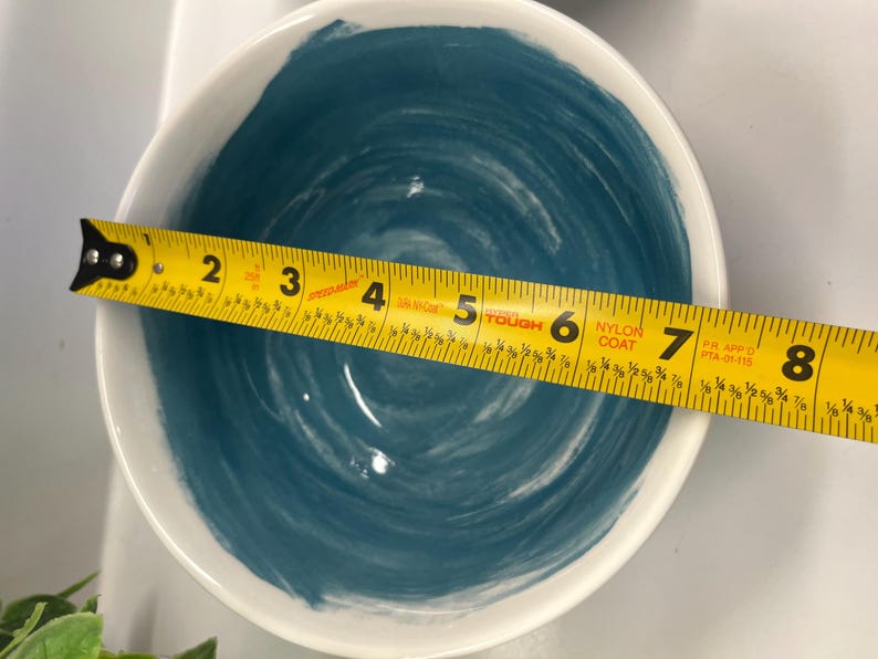 May include: White ceramic bowl with a blue swirl design. A yellow tape measure is placed across the bowl, showing a diameter of approximately 18 cm.
