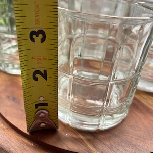 Puede incluir: Conjunto de cuatro vasos transparentes de vidrio con un patr&oacute;n de cuadr&iacute;cula. Los vasos est&aacute;n sobre una superficie de madera. Se puede ver una cinta m&eacute;trica en la imagen, que muestra que la altura de los vasos es de 8,26 cm.