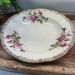 May include: White porcelain bowl with a scalloped edge and gold trim. The bowl features a floral design of pink roses and green leaves. A vintage-style serving dish for soups or salads.