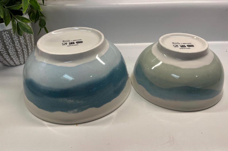 May include: Two ceramic bowls with a white base and a blue and teal watercolour design. The bowls are different sizes and have a glossy finish. The bowls are suitable for serving food.