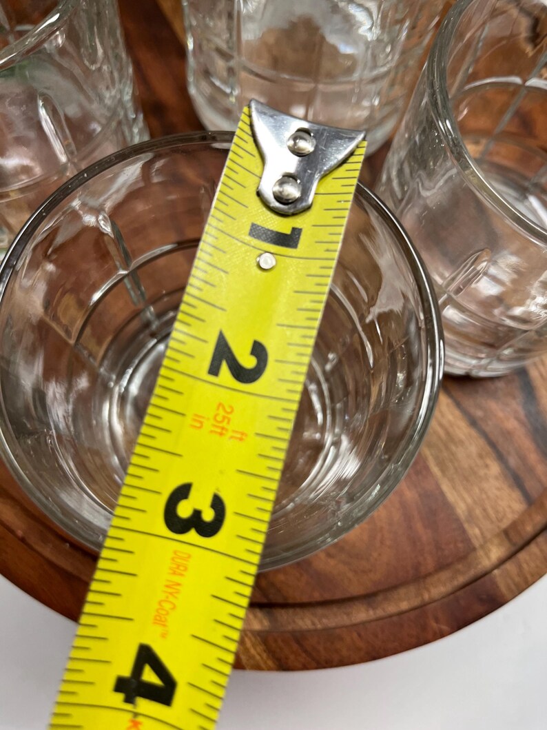 Puede incluir: Cuatro vasos transparentes de vidrio con un dise&ntilde;o texturizado, medidos con una cinta m&eacute;trica amarilla. La cinta m&eacute;trica indica 3 pulgadas.