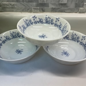 May include: Three white ceramic bowls with a blue floral pattern around the rim and a smaller floral design in the center. The bowls are oval-shaped and sit on a white surface.