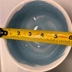 May include: A white ceramic bowl with a blue interior and a white rim. The bowl is approximately 15 cm in diameter. The blue paint has a brushstroke texture.