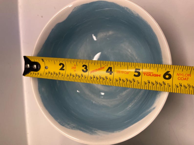 May include: A white ceramic bowl with a blue interior and a white rim. The bowl is approximately 15 cm in diameter. The blue paint has a brushstroke texture.