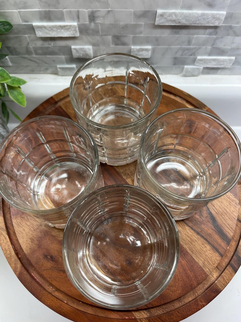 Puede incluir: Cuatro vasos transparentes de vidrio con un dise&ntilde;o texturizado y acanalado. Los vasos est&aacute;n dispuestos sobre una superficie de madera.