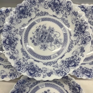 May include: A collection of white porcelain plates with a blue floral design. The plates have a scalloped edge and a detailed pattern of roses and other flowers. The center of each plate features a floral bouquet design.