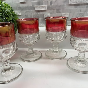 May include: Set of four clear glass goblets with a ruby red iridescent finish. The goblets have a round bowl and a tall, slender stem with a wide base.