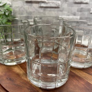 Puede incluir: Cuatro vasos transparentes de vidrio con un patr&oacute;n de rejilla. Los vasos est&aacute;n sobre una superficie de madera.