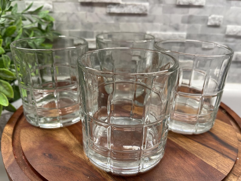 Puede incluir: Cuatro vasos transparentes de vidrio con un patr&oacute;n de rejilla. Los vasos est&aacute;n sobre una superficie de madera.