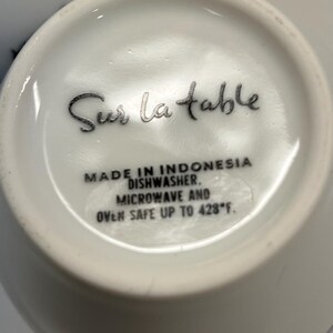 Puede incluir: Taza de cer&aacute;mica blanca con el texto "Sur la table" en escritura negra. La base de la taza incluye texto que indica que est&aacute; hecha en Indonesia, es apta para lavavajillas y microondas, y resistente al horno hasta 220&deg;C.