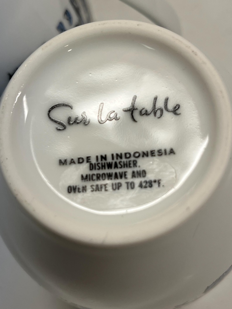 Puede incluir: Taza de cer&aacute;mica blanca con el texto "Sur la table" en escritura negra. La base de la taza incluye texto que indica que est&aacute; hecha en Indonesia, es apta para lavavajillas y microondas, y resistente al horno hasta 220&deg;C.