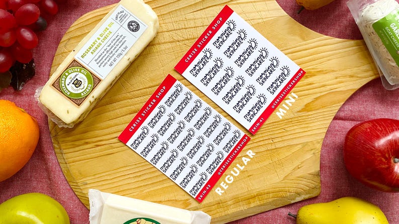 May include: Two sheets of stickers with the text "Morning Skincare" printed on them. The stickers are on a wooden cutting board with a block of cheese, grapes, an orange, an apple, and a pear.