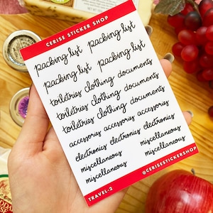Peut inclure: Une feuille d'autocollants blanche avec le texte "packing list" répété plusieurs fois en écriture cursive noire. La feuille d'autocollants comprend également les mots "toiletries", "clothing", "documents", "accessories", "electronics" et "miscellaneous" en écriture cursive noire. La feuille d'autocollants est étiquetée "TRAVEL-2" dans le coin inférieur gauche et "@CERISESTICKERSHOP" dans le coin inférieur droit.