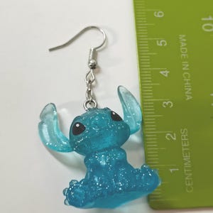 Pu&ograve; includere: Un singolo orecchino Stitch blu glitterato con un gancio argentato. L'orecchino &egrave; alto circa 5 cm. L'orecchino &egrave; realizzato in un materiale blu traslucido con occhi neri.
