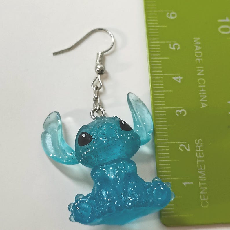 Pu&ograve; includere: Un singolo orecchino Stitch blu glitterato con un gancio argentato. L'orecchino &egrave; alto circa 5 cm. L'orecchino &egrave; realizzato in un materiale blu traslucido con occhi neri.