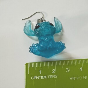 Pu&ograve; includere: Un orecchino Stitch blu glitterato con un gancio d'argento. L'orecchino &egrave; alto circa 2,5 cm. L'orecchino &egrave; un personaggio dei cartoni animati con grandi orecchie e un corpo rotondo.