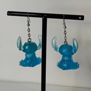 Pu&ograve; includere: Un paio di orecchini Stitch blu glitterati. Ogni orecchino presenta una piccola e dettagliata figura di Stitch con grandi orecchie e una posa seduta. Gli orecchini pendono da ganci per orecchie color argento.