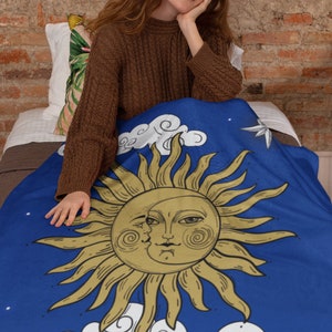 Könnte beinhalten: Eine blaue Decke mit einer weißen Wolke und einer goldenen Sonne mit einem Gesicht. Die Sonne hat eine sichelförmige Mondform auf ihrem Gesicht. Die Decke hat ein Muster aus weißen Sternen.
