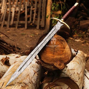 May include: A long, silver sword with a brown leather handle and a gold-coloured pommel. The sword is resting on a wooden log.
