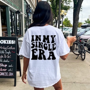 May include: White oversized t-shirt with black text that reads "IN MY SINGLE ERA" in a retro font.
