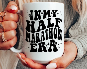 May include: White ceramic mug with black text that reads "In My Half Marathon Era" with small flower and star designs.