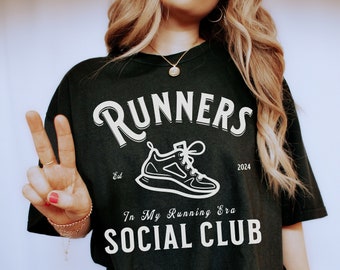 Puede incluir: Camiseta negra con texto blanco que dice "RUNNERS Est. 2024 In My Running Era SOCIAL CLUB" y una ilustración blanca de una zapatilla para correr.