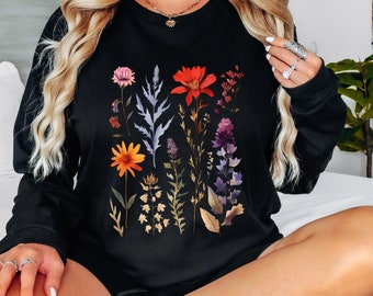 May include: Black long-sleeved sweatshirt with a floral print featuring a variety of flowers and leaves in shades of red, orange, yellow, purple, and blue.