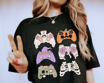 Op de afbeelding: Zwart T-shirt met een afbeelding van zes verschillende Halloween-videogamecontrollers. De controllers zijn versierd met geesten, pompoenen, heksen, mummies, zombies en skeletten.