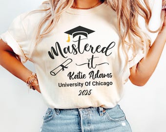 May include: Ivory-colored t-shirt with the text "Mastered it" and a graduation cap graphic. The shirt also includes the name "Katie Adams", "University Of Chicago", and the year "2025".