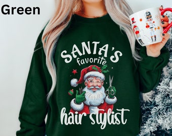 Op de afbeelding: Bostgroene sweatshirt met de tekst "SANTA'S favorite hair stylist" en een afbeelding van de Kerstman met een schaar. De sweatshirt heeft een effen bosgroene kleur.