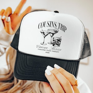May include: Black and white trucker hat with the text "COUSINS TRIP Cancun, Mexico CHEAPER THAN THERAPY 2025" and illustrations of cocktails. The hat has a black brim and mesh back.