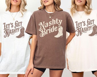 Può includere: Tre magliette a tema country. Le magliette sono bianche e marroni, con le scritte "Let's Get Nashty" e "Nashty Bride" stampate, insieme a una grafica di stivale da cowboy. Le magliette sono a maniche corte e hanno una vestibilità ampia.