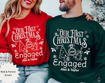 May include: Red and forest green sweatshirts with the text "Our First Christmas Engaged" in white. The design includes a Christmas tree, a diamond ring, and a champagne bottle. The names "Alex & Taylor" are printed below.