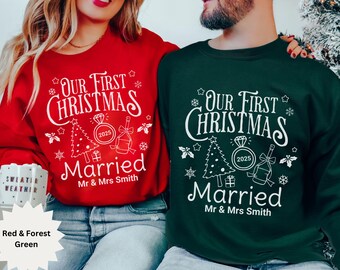 Può includere: Felpe natalizie rosse e verde foresta con la scritta "Our First Christmas Married" e l'anno 2025. Il design include un albero di Natale, un anello e una bottiglia di champagne. Un regalo festivo per le vacanze.