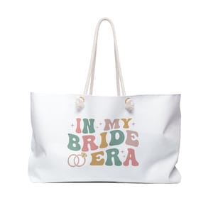 May include: White canvas tote bag with a colorful graphic that says "In My Bride Era" with two gold rings and a diamond.